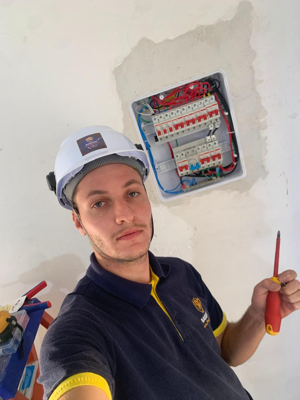 Eletricista da Bassani com capacete ao lado de quadro de distribuição recém-instalado, com fiação organizada por cores