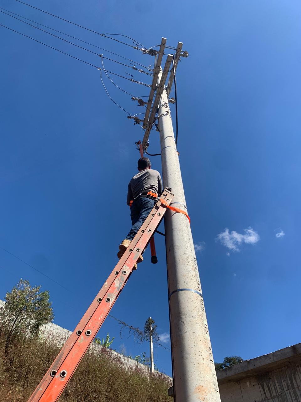 Eletricista em escada realizando manutenção em poste